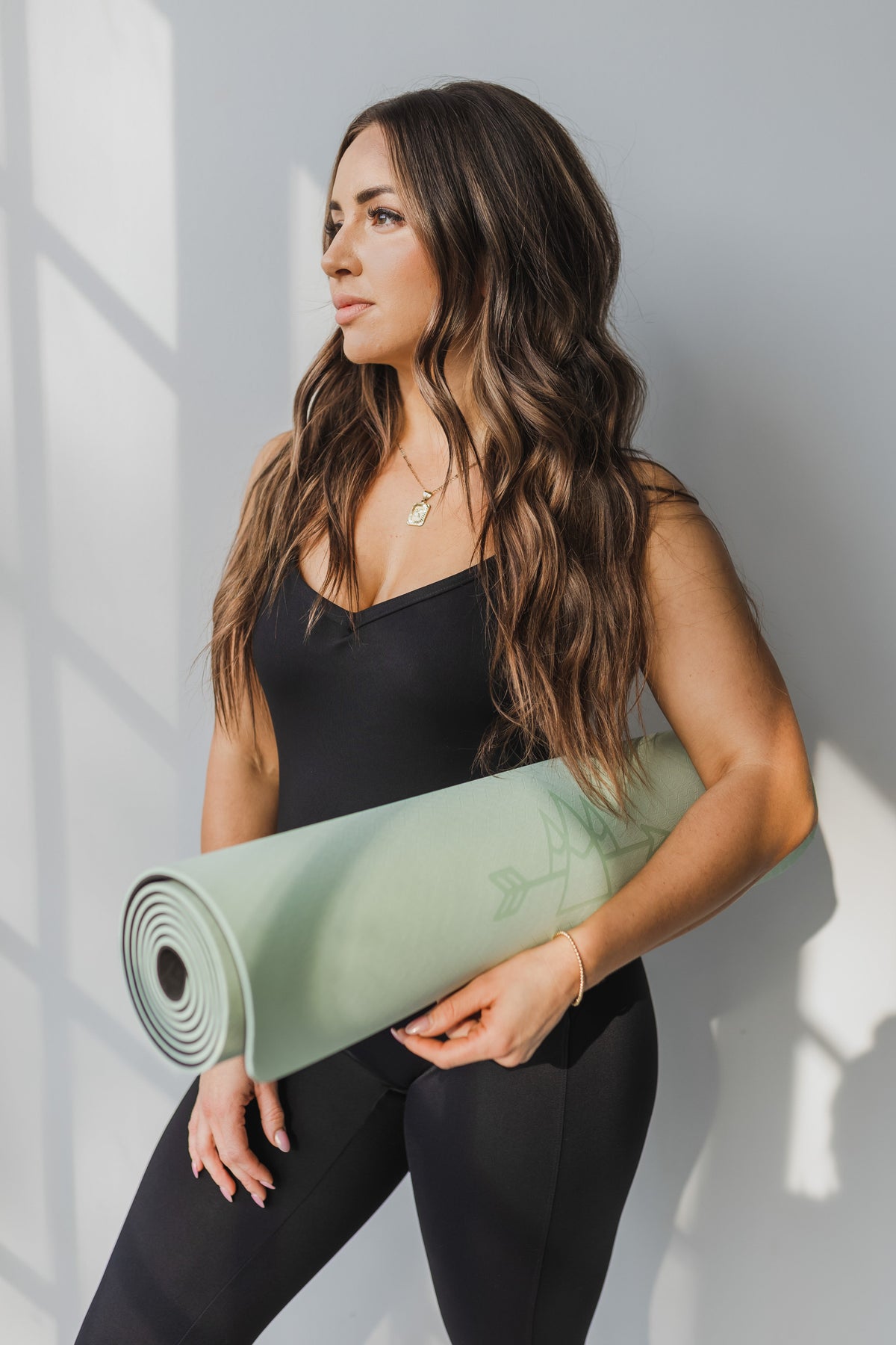 Femme tenant un tapis de yoga enroulé menthe près d'un mur blanc