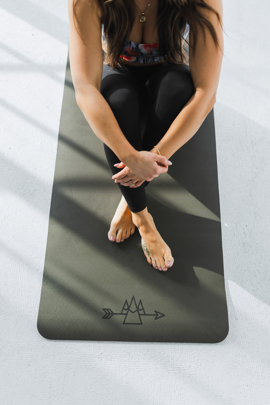 Femme assise sur un tapis de yoga noir avec logo