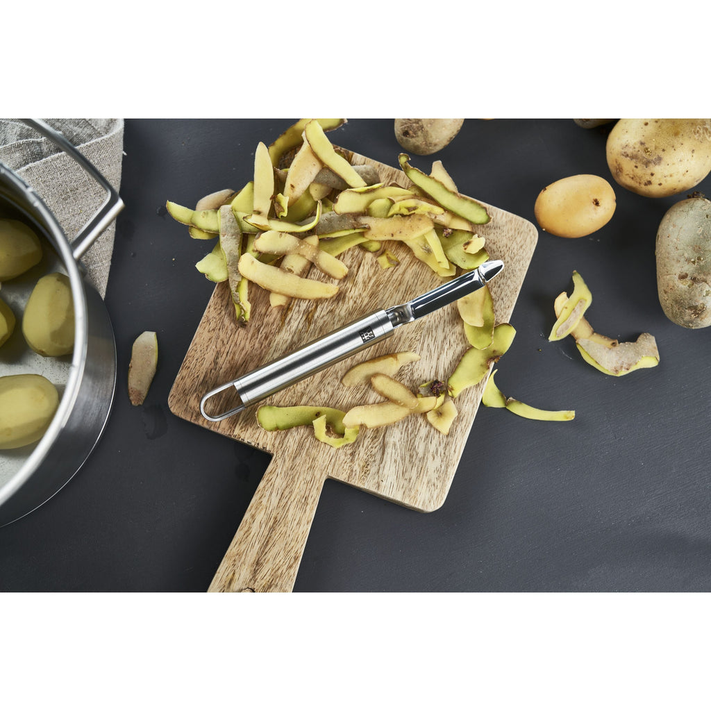 Éplucheur pivotant ZWILLING Pro sur une planche à découper avec des épluchures de pommes de terre