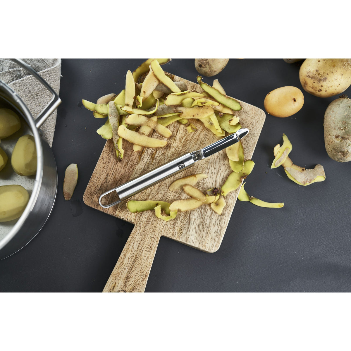 Éplucheur pivotant ZWILLING Pro sur une planche à découper avec des épluchures de pommes de terre