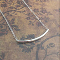 Collier en argent sterling avec barre incurvée, posé sur un tissu à motifs floraux